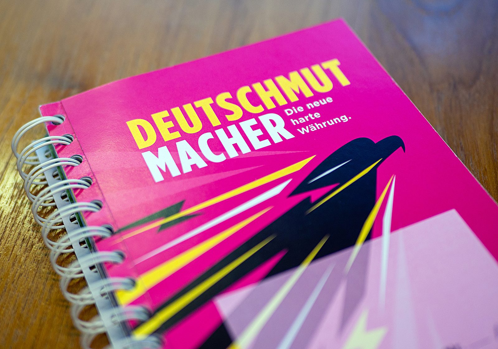 Paper-Dummy der Collector’s Edition DEUTSCHMUT MACHER: magentafarbenes Klappbuch mit Wire-O-Bindung auf Holztisch