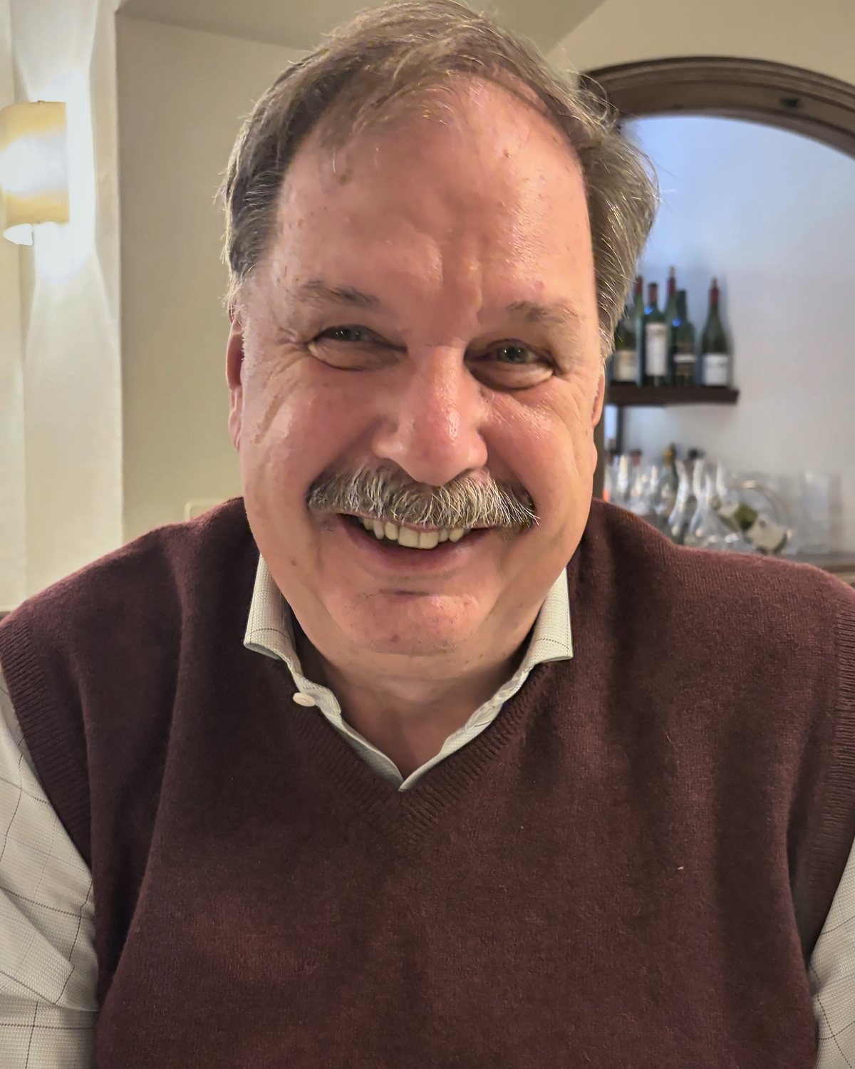 Gerhard Müller, lachend, in einem Lokal mit Weinregal im Hintergrund